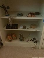 Shelf view of travel souvenirs including metal warrior statue, stone mask, wooden turtle, mini dolls, wooden clogs, and other small items.