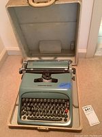Full view of the teal blue Underwood Olivetti manual typewriter inside a hard carrying case, showing the full keyboard and platen roller.