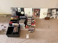 Overall lot showing vinyl records against wall, various CDs, DVDs, cassette tapes, and organizers arranged on carpet.