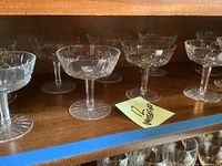 Twelve Waterford Lismore sherbet glasses arranged on a wooden shelf, showing varying stem thickness and weights.