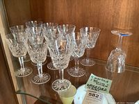 Twelve wine glasses displayed on glass shelf. Eleven marked Waterford, one unmarked and damaged. Mixed stem thickness and weights visible.