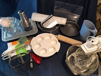 Photo showing assortment of baking tools including stand mixer, measuring spoons, cake pans, rolling pin, and egg holder.