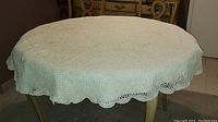 Round warm white hand-crocheted table cloth draped over a wooden table, showing overall size and scalloped edges
