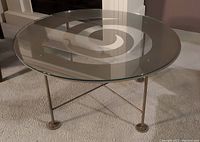 View of the round glass tabletop and metal base with swirl cut-out design from side angle.