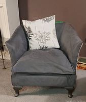 Front view of the club chair with grey ultrasuede upholstery and botanical print pillow.
