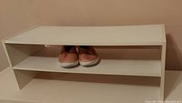 Front view of the white particle board shoe shelf with two compartments; shoes placed on bottom shelf not included
