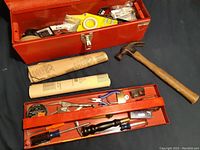 Photo of red metal toolbox open with tools inside and hammer beside it
