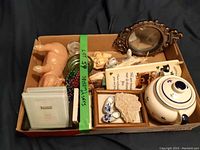 Box containing small trinkets including photo frames, ceramic garlic holder, bells, and decorative mirror