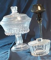 Photo showing 10-inch lidded pedestal cut glass candy dish, Reese's crystal dish with lid, and tall two-toned candle holder alongside glass votive.