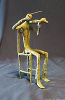 Front and side view showing the violin player playing the violin seated on chair with elongated limbs in bronze with green patina.