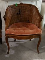 Front view of wooden framed wicker chair with rose velvet cushion, showing tufted cushion and damage to wicker back.
