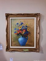 Full view of framed floral painting showing vibrant bouquet of yellow, orange, and blue flowers in a blue vase with ornate frame.
