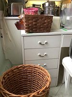 Wicker baskets in front of white drawer unit, showing large and medium baskets and part of wood tray and bread box in background