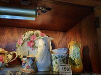 Shelf display showing Belleek vase, Royal Worcester egg holder, and other porcelain items including bowls and brush holder.