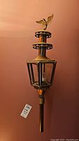 Photo of single candle sconce, showing brass eagle finial top, hexagonal glass enclosure, and metal body