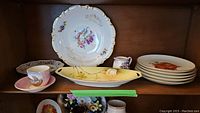 Wide view showing assortment of plates, cups, and decorative dish on shelf