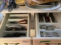 Overview of two kitchen drawers containing assorted cutlery and utensils separated by compartments showing forks, spoons, knives, and kitchen tools.
