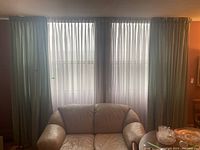 Photo of four drapery panels hanging over a window behind a beige leather sofa, showing two sheer white panels in the middle and two heavier beige panels on the sides.