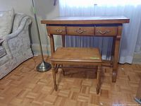 Dressing table with three drawers and matching stool in front. Wood finish medium brown. Set against wall with curtain background.