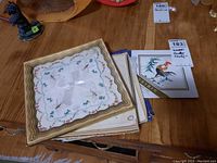 Various handkerchiefs laid out on table, showing multiple folded pieces with different decorative edges and hand-drawn silk designs.