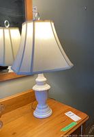 Full view of the white ceramic base lamp with fabric shade on a wooden dresser, showing its overall size and shape.