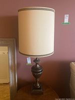 Tall vintage Stiffel lamp with cream textured fabric shade and dark decorative metal base on wooden side table.