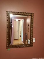 Full view of the rectangular mirror with ornate carved painted frame against a wall.