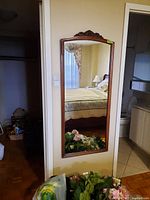 Full front view of the wood framed vertical wall mirror reflecting a bedroom.