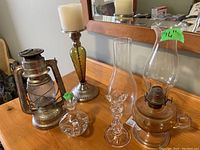 Photo of the complete set including metal oil lantern, glass candle holders, perfume bottle, and glass chimney on wooden table.
