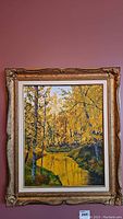 Full view of the framed oil painting on board showing a forest scene with trees, river, and yellow autumn leaves against a light sky.