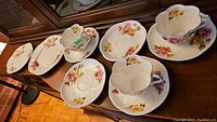 Overview of three floral teacups with five saucers and two plates, showing chip on one cup
