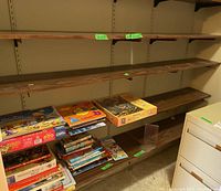 Photo showing three veneer shelves mounted with metal hook supports, with various books and puzzles placed on the bottom shelf.