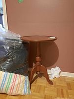 Full view of brown wood round side table next to bags and wall.