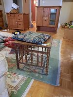 Overall view of wooden side table with cushion on top, showing spindled legs and surrounding room