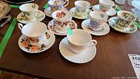 Nine assorted vintage teacups and saucers displayed on a wooden table with varied floral patterns and colors