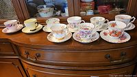 Full set of nine floral teacups and saucers displayed on wooden surface