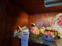Porcelain tea set and decorative items displayed on glass shelf with price tag visible