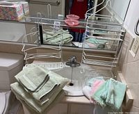 Two pale green towels, hand towels, washcloths, two white metal shower racks on bathroom counter.