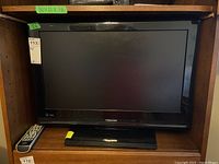 Full front view of Toshiba 26 inch LCD television on stand with remote on the shelf to the left