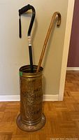 Full view of umbrella stand holding two canes against wall and wood floor