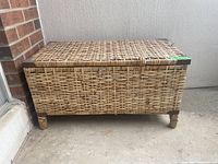 Full front view of the weathered wicker chest showing woven wicker panels and wooden legs, closed lid.