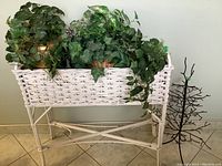 White wicker planter holding brass planter with faux ivy plants inside, shown from front view