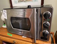 Front view of the Wolfgang Puck Kitchtek Pressure Oven showing its stainless steel body, front glass window, and three black control knobs on the right side.
