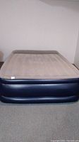 Queen size Ozark Trail air mattress shown inflated with beige top and dark blue sides, set against a plain white wall.