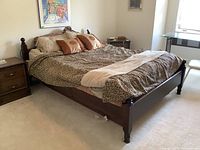 Full view of bed showing leopard pattern bedding, pillows, and hardwood frame with turned legs.