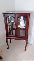 Front view of wood cabinet with glass door showing the dark wood, glass panels, and curved legs.
