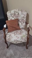 Front view of upholstered tufted back wooden chair with floral upholstery and brown throw cushion on seat
