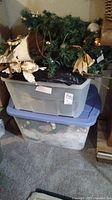 Stacked plastic storage bins containing the Christmas decorations and the garland with some components visible
