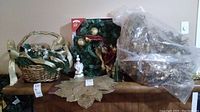 Christmas decorations including two wicker baskets with faux greenery and gold ribbon bows, a green wreath with gold ornaments and a red and gold bow, two white ceramic snowman soap dispensers, and a gold poinsettia placemat.