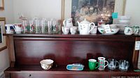Wide shot of all Christmas dishware and glassware arranged on wooden cabinet with various cups, bowls, plates, teapot, and glasses.